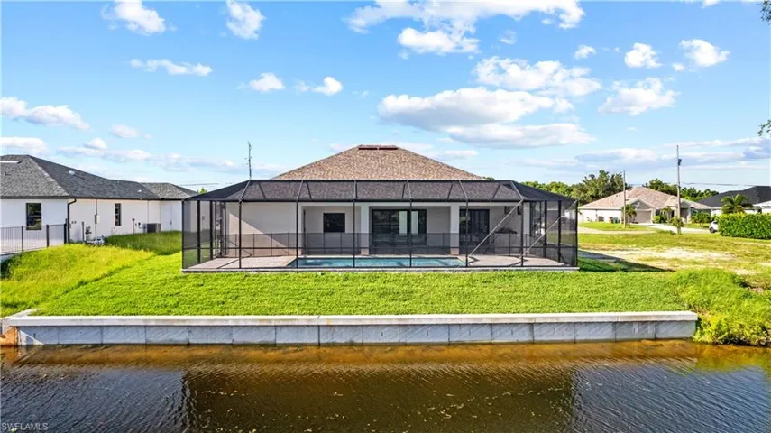 Rear view of property with a water view, a yard, a patio area, and a lanai