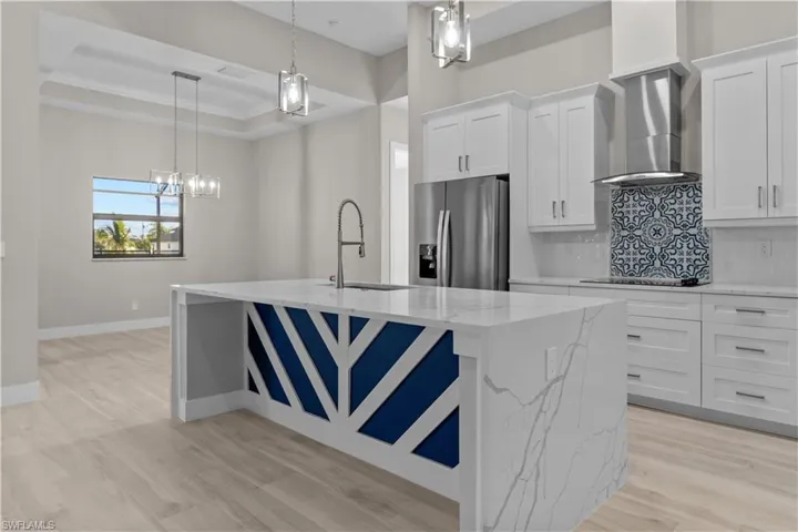 Kitchen with appliances with stainless steel finishes, tasteful backsplash, wall chimney range hood, light wood-type flooring, and white cabinetry