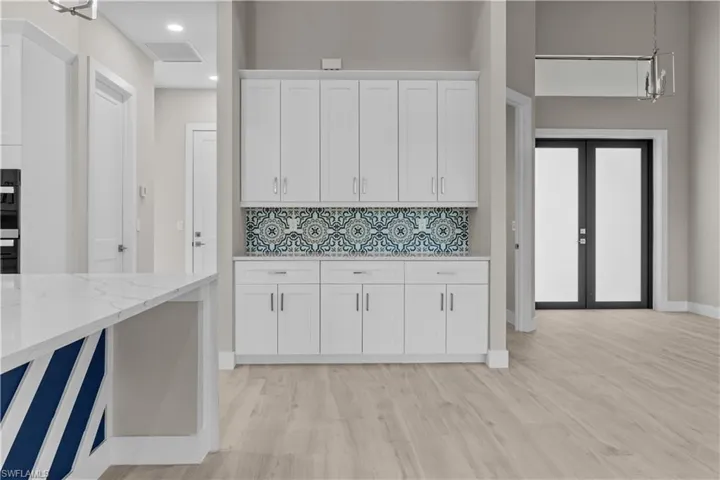 Kitchen with white cabinetry, light stone counters, light hardwood / wood-style floors, decorative backsplash, and decorative light fixtures