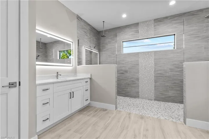 Bathroom featuring tiled shower, vanity, and a wealth of natural light