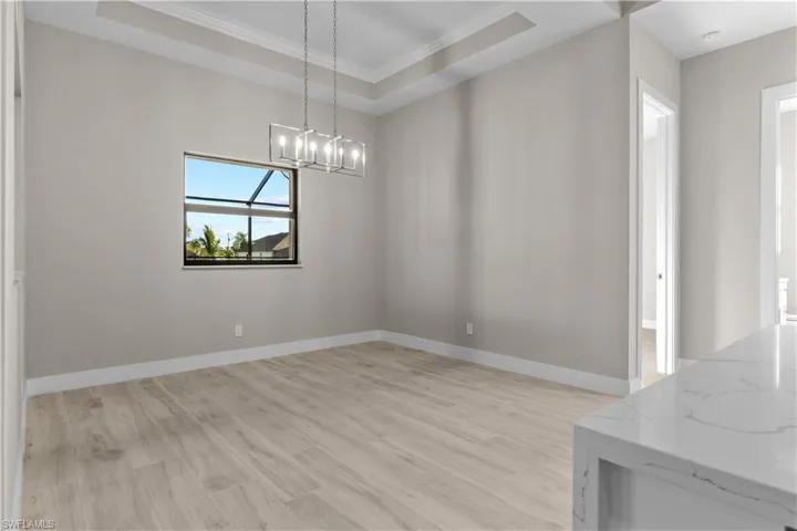 Dining room with an inviting chandelier, light hardwood / wood-style flooring, ornamental molding, and a tray ceiling