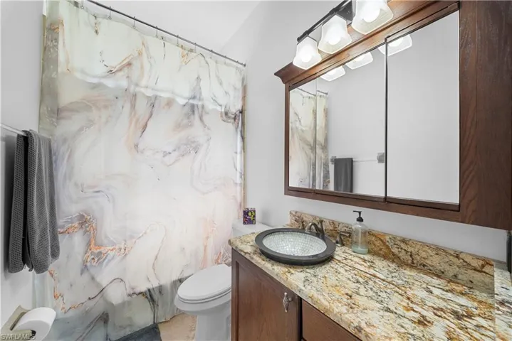 Bathroom featuring a wood-finish vanity with a stone countertop, an integrated vessel sink, and a triple-mirror medicine cabinet with integrated lighting