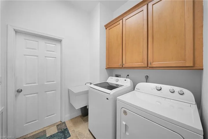 Laundry room featuring neutral-toned tile flooring, wall-mounted natural wood cabinetry, and a wall-mounted utility sink