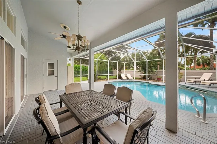 Covered patio with brick-pattern flooring, in-ground swimming pool, screened-in enclosure, and multi-arm chandelier