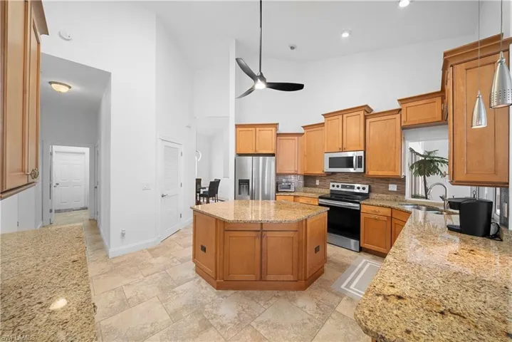Kitchen featuring an octagonal central island, stone-surfaced countertops, wood cabinetry, stainless steel appliances, and tile flooring under vaulted ceilings