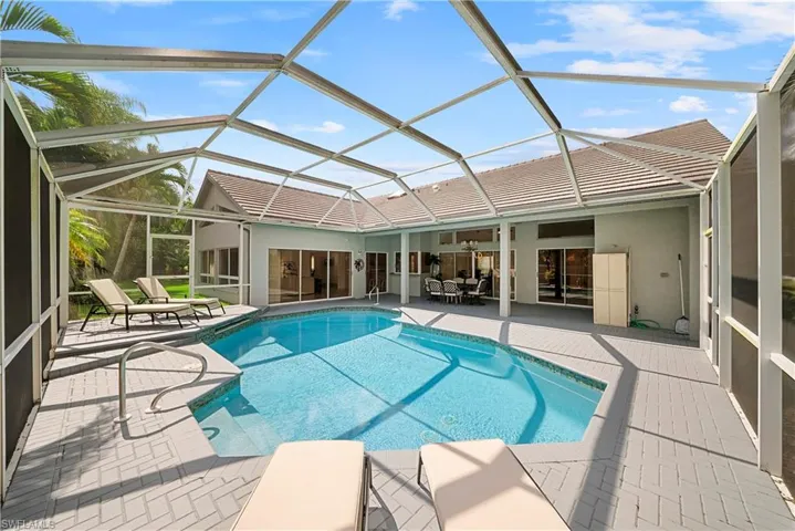 Screened-in patio featuring a swimming pool, herringbone-patterned paved decking, and multiple sliding glass door access points