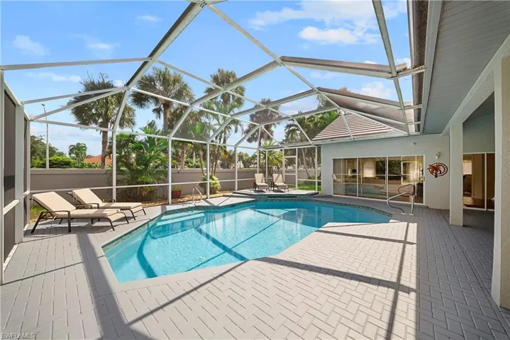Screen-enclosed pool area featuring concrete paver decking, a raised platform step, and a perimeter wall
