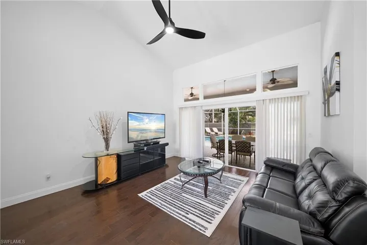 High-vaulted ceilings, dark wood-finish flooring, matte black three-blade ceiling fan, and oversized sliding glass doors with transom windows