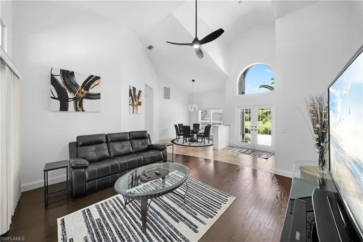 Vaulted ceilings, wood-finish flooring, an arched window, a modern three-blade ceiling fan, and double-entry glass doors