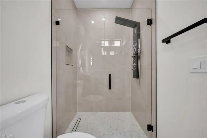 Glass-enclosed shower with a modern shower panel system, integrated niche, and light-toned tile surround