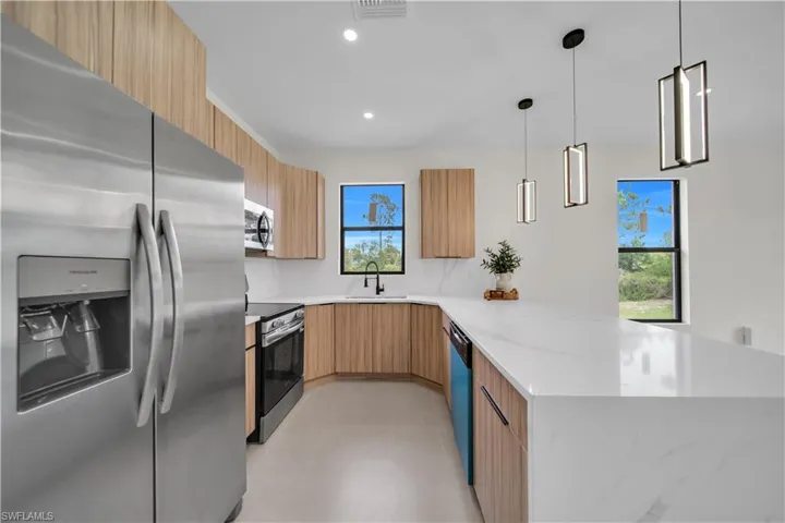 Contemporary kitchen featuring stainless steel appliances, light wood-finish cabinetry, a waterfall-edge island, and pendant lighting fixtures