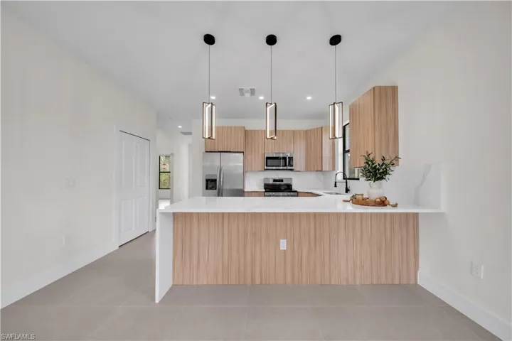 Contemporary kitchen with wood-finish cabinetry, stainless steel appliances, and a white countertop island with pendant lighting