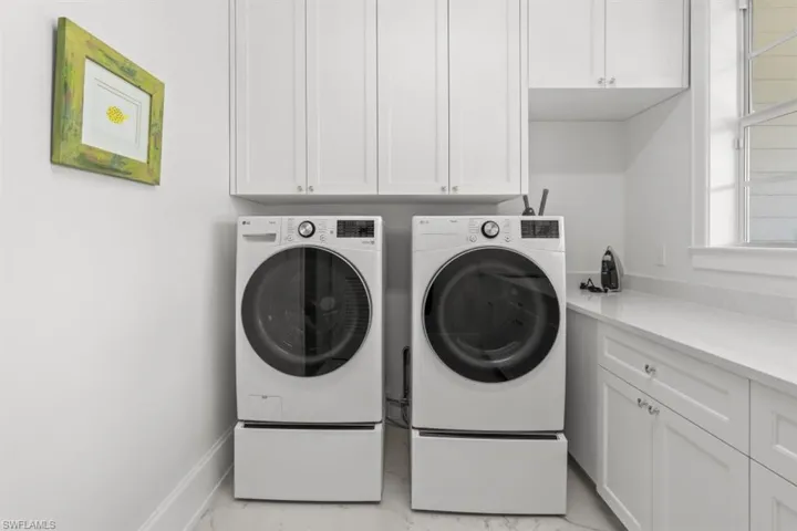 Laundry area featuring independent washer and dryer, cabinet space, and light marble finish flooring
