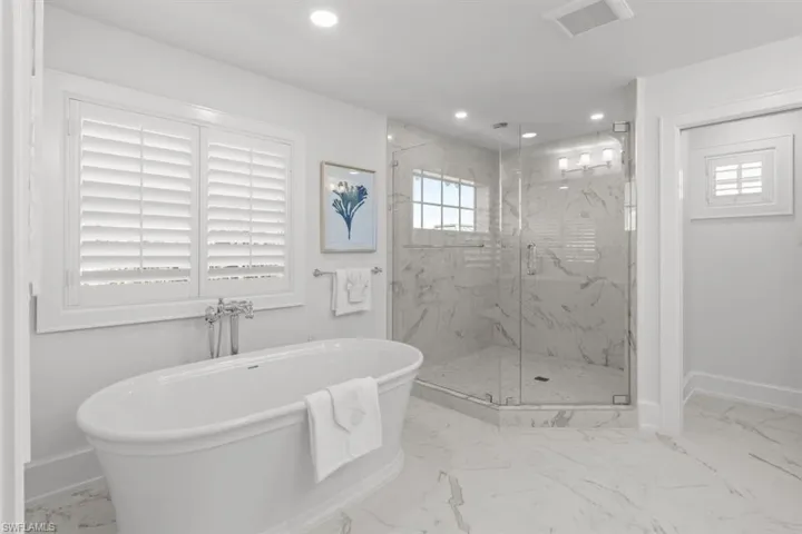 Bathroom featuring light marble finish floors, a freestanding bath, a marble finish shower, and recessed lighting