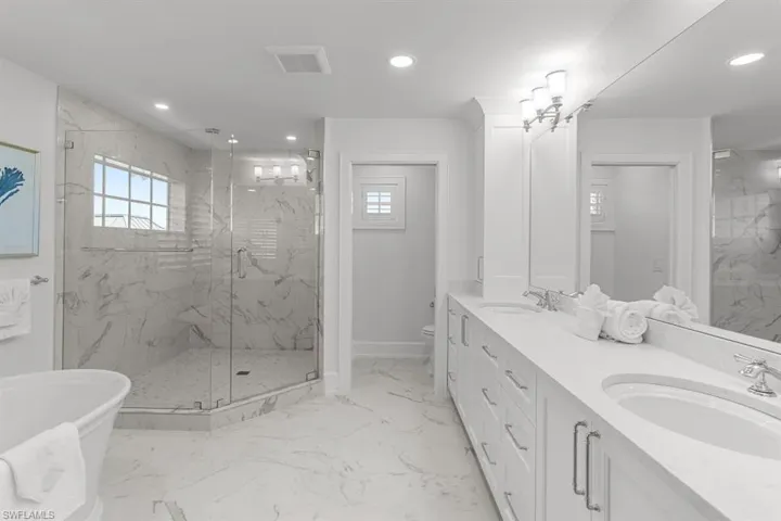 Full bathroom featuring light marble finish flooring, a marble finish shower, recessed lighting, double vanity, and a freestanding tub