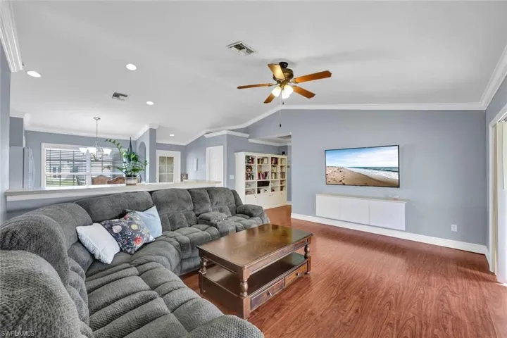 Living room with Vaulted ceiling, hardwood wood-style laminate floors, ornamental molding, and ceiling fan.
