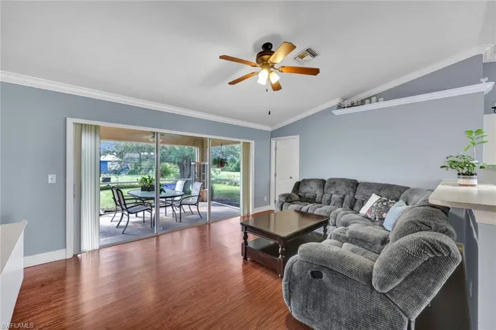Living room with ornamental molding, ceiling fan, vaulted ceiling, and sliders out to the screened patio