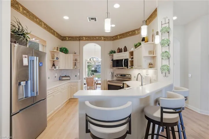 Kitchen with stainless steel appliances, light countertops, light wood-style flooring, pendant lighting, and backsplash