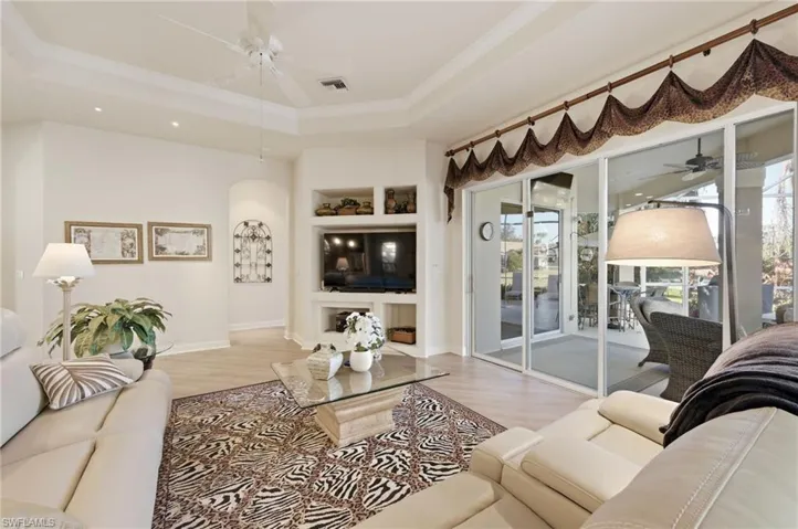Living area featuring ceiling fan, built in features, wood finished floors, crown molding, and a tray ceiling