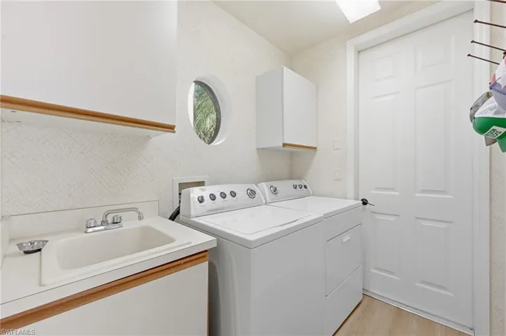Laundry area featuring light wood-type flooring, cabinet space, washing machine and clothes dryer, and a textured wall