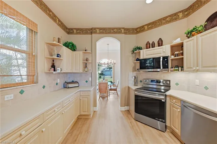Kitchen with stainless steel appliances, open shelves, decorative backsplash, light wood-type flooring, and a chandelier