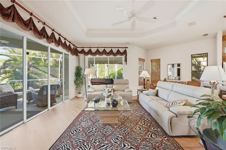 Living area with wood finished floors, a ceiling fan, plenty of natural light, crown molding, and a tray ceiling