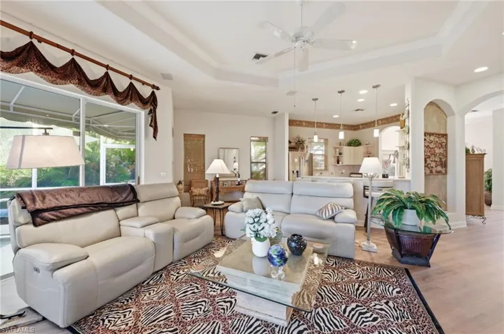 Living room featuring wood finished floors, a ceiling fan, crown molding, a tray ceiling, and arched walkways