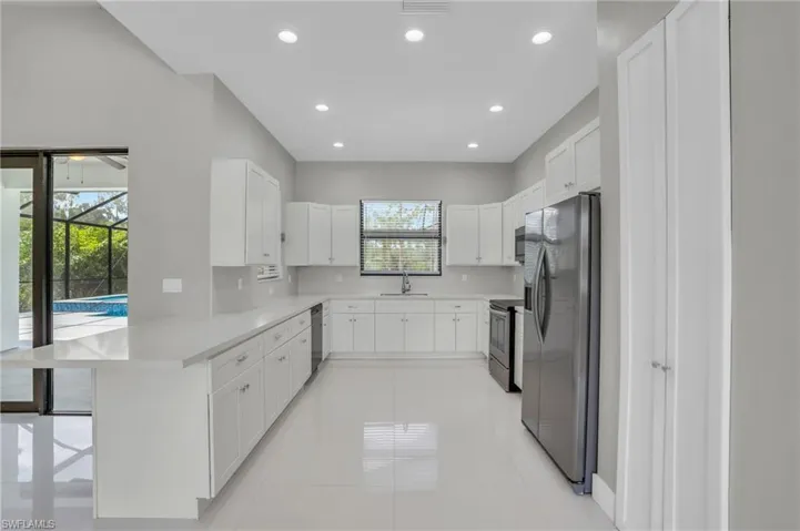Kitchen with stainless steel appliances, light tile flooring, sink, white cabinets, and a breakfast bar area