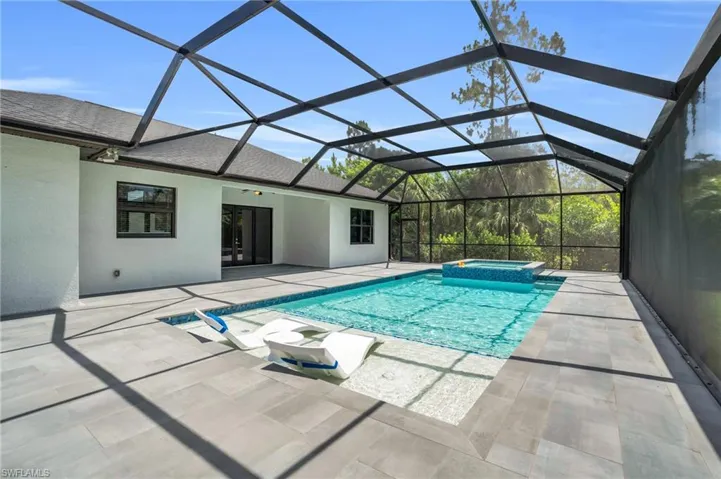 View of swimming pool with a patio, glass enclosure, and an in ground hot tub