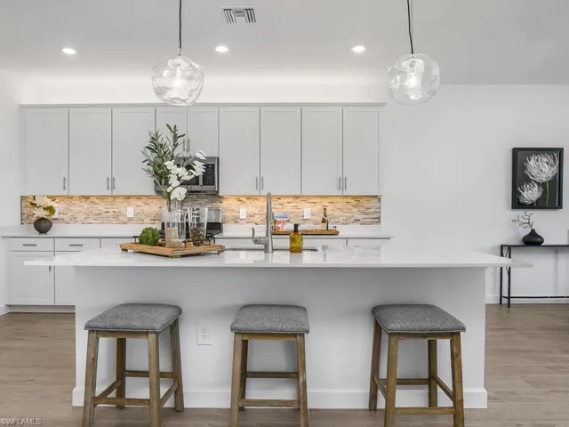 Open Kitchen/Dining space featuring glass tile backsplash, designer pendant lighting, quartz countertops and oversized island.