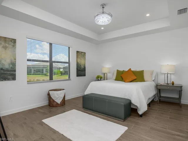 Owner suite is spacious with wood-like plank tile flooring, tray ceilings with after-market recessed lighting, chandelier with fan, and a great view of the water.