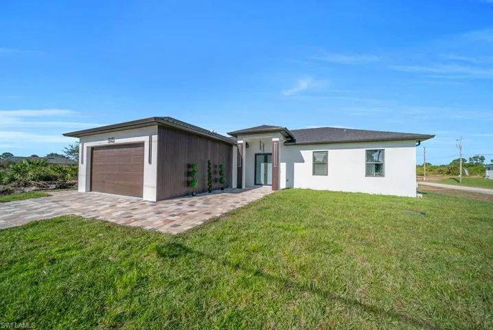 Prairie-style home featuring an attached garage, a front yard, stucco siding, and decorative driveway