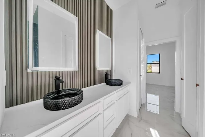Bathroom featuring light marble finish flooring, double vanity, and wallpapered walls