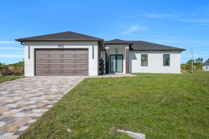 View of front facade featuring stucco siding, a front lawn, decorative driveway, and a garage