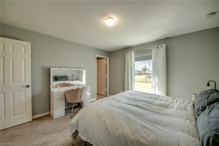 Bedroom featuring neutral wall paint, wall-to-wall carpeting, a single-panel interior door, and a window with a curtain rod fixture