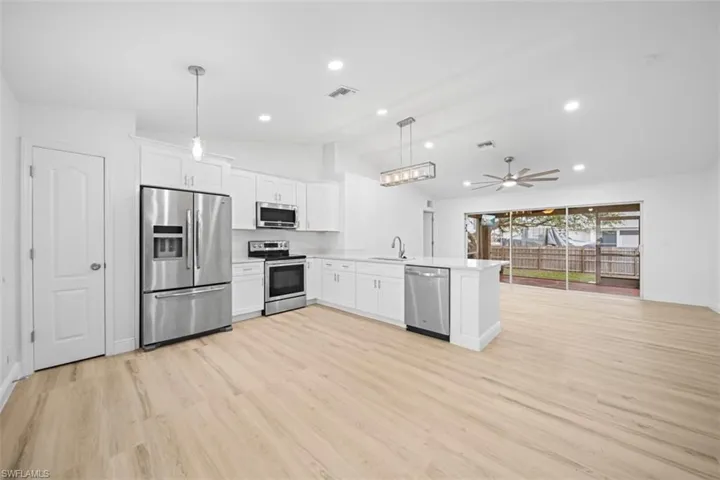 Kitchen featuring stainless steel appliances, white cabinets, ceiling fan, hanging light fixtures, and open floor plan