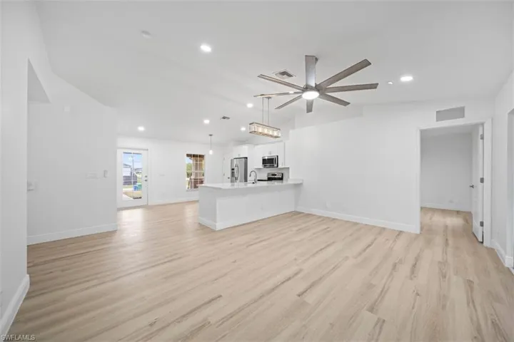 Unfurnished living room with light wood finished floors, ceiling fan, vaulted ceiling, and recessed lighting