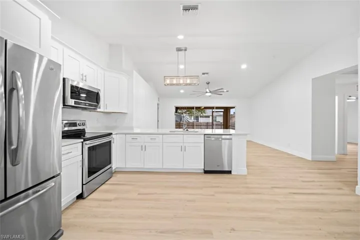 Kitchen featuring stainless steel appliances, white cabinets, a peninsula, lofted ceiling, and light wood-style floors
