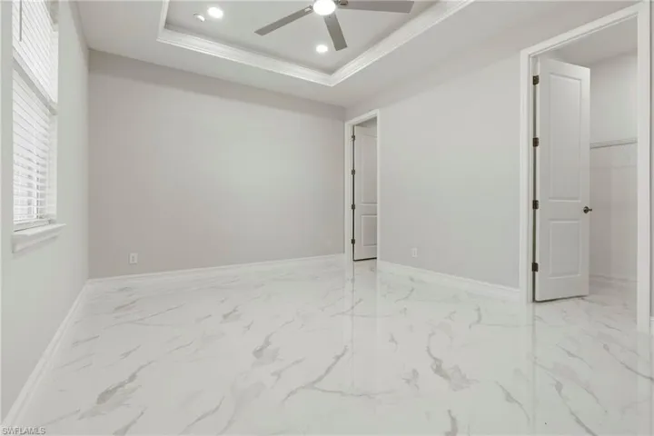 Spare room with a tray ceiling, marble finish floor, recessed lighting, ceiling fan, and baseboards