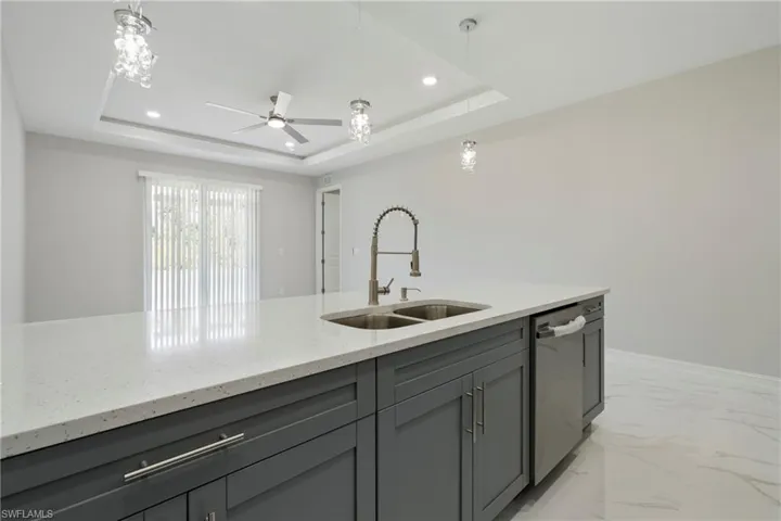 Kitchen with a sink, marble finish floor, stainless steel dishwasher, gray cabinets, and a raised ceiling