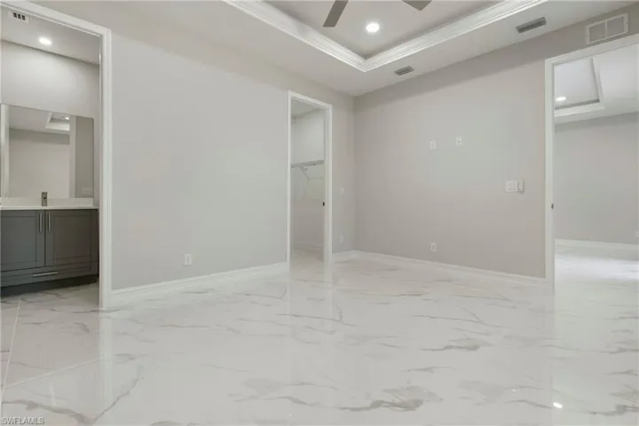 Empty room with a tray ceiling, marble finish floor, visible vents, and crown molding