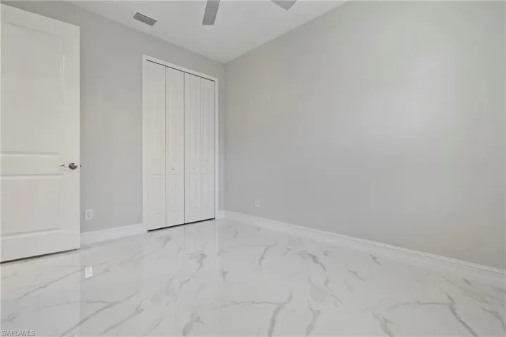Unfurnished bedroom with a ceiling fan, visible vents, baseboards, marble finish floor, and a closet