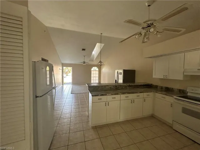 Kitchen with ceiling fan, white appliances, open floor plan, dark countertops, and vaulted ceiling