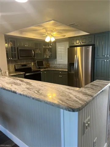 Kitchen with stove, tasteful backsplash, light stone counters, fridge, and ceiling fan