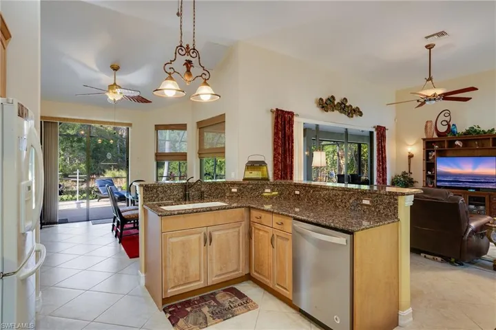 Kitchen featuring a ceiling fan, white fridge with ice dispenser, stainless steel dishwasher, dark stone counters, and open floor plan