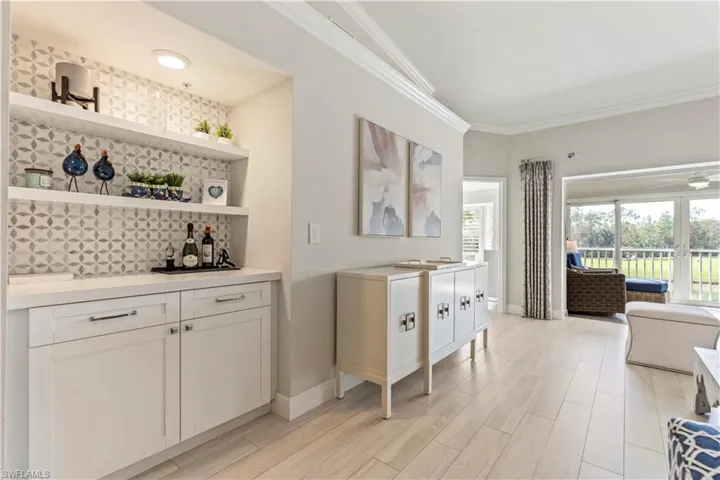 Bar with baseboards, a dry bar, ornamental molding, and light wood finished floors