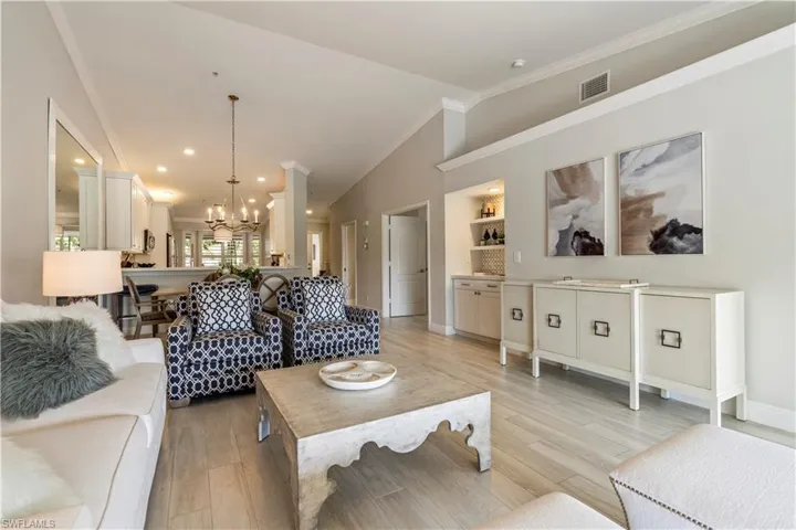 Living area featuring visible vents, crown molding, light wood finished floors, an inviting chandelier, and vaulted ceiling