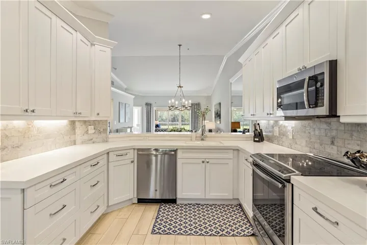 Kitchen with white cabinetry, ornamental molding, stainless steel appliances, a sink, and a notable chandelier