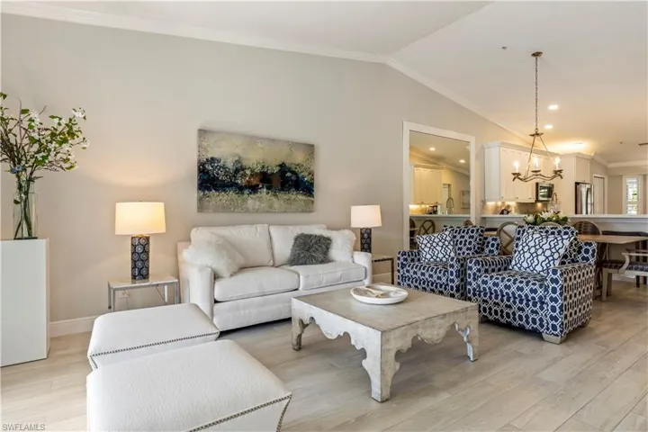 Living area with a notable chandelier, crown molding, lofted ceiling, light wood-type flooring, and baseboards
