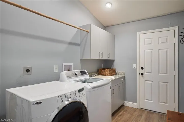 Laundry room featuring separate washer and dryer, cabinets, light wood-type flooring, and sink